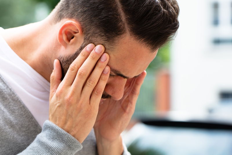 CBD bei Migräne: Natürliche Hilfe gegen den Schmerz Mann mit Migräne hält sich schmerzhaft die Schläfen – mögliche Linderung durch CBD-Produkte