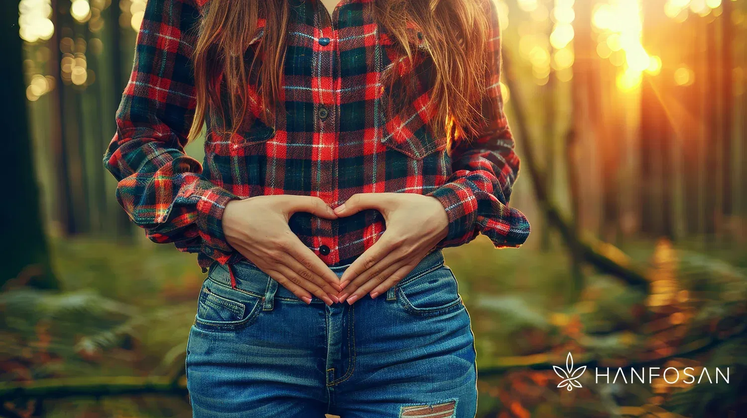Gesunder Darm, starkes Immunsystem – natürliche Balance mit Hanfosan Frau im karierten Hemd formt mit den Händen ein Herz über dem Bauch, stehend im herbstlichen Wald, Hanfosan-Logo unten rechts sichtbar