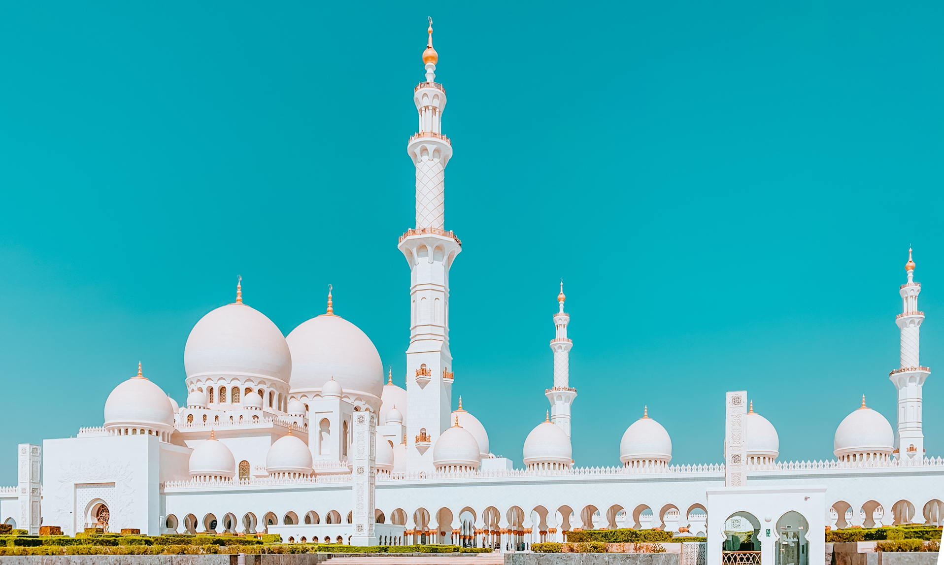 Weiße Moschee mit goldenen Kuppeln und Minaretten vor klarem türkisfarbenem Himmel, Symbolbild für Religion und spirituelle Vielfalt