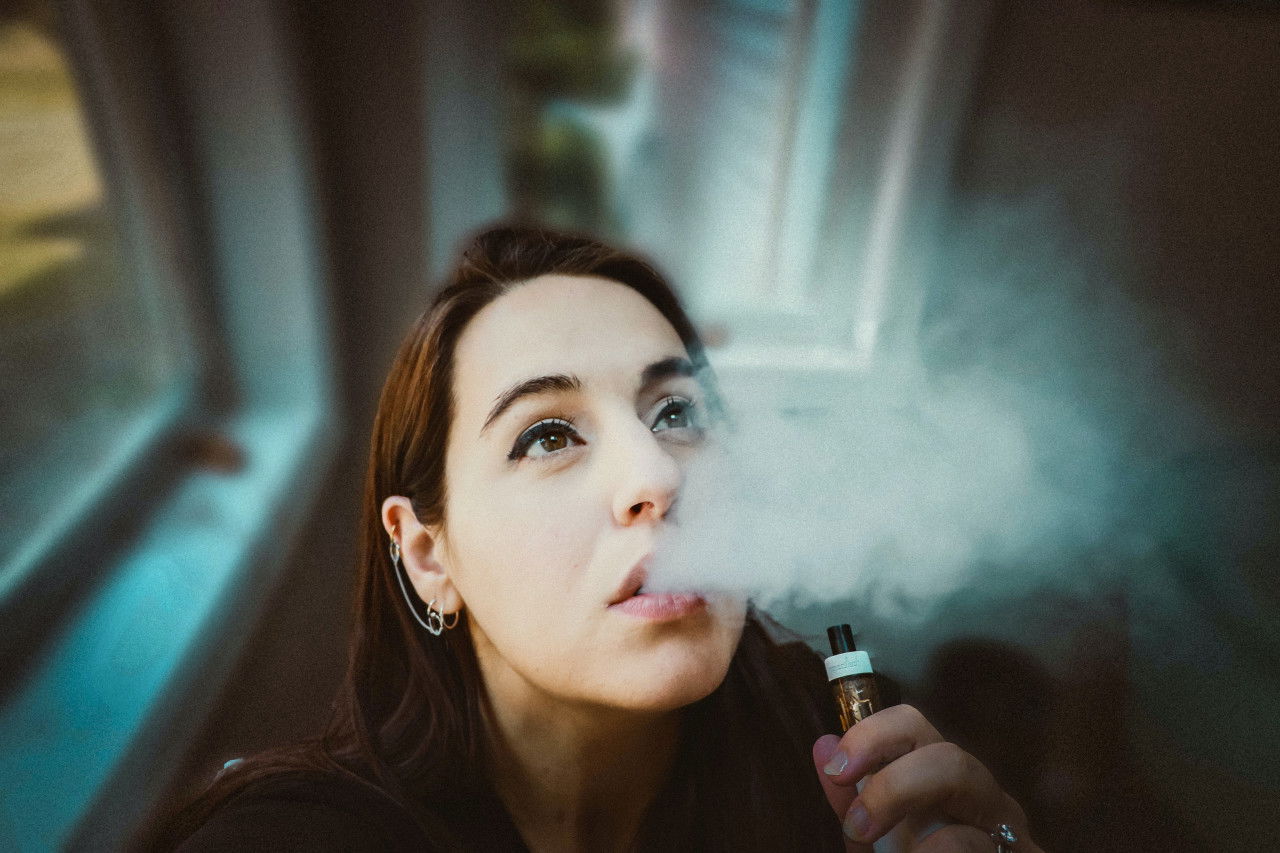 Frau beim Dampfen eines CBD Vape Pens in entspannter Atmosphäre Junge Frau inhaliert CBD-Dampf mit einem Vape Pen in einem hellen Raum
