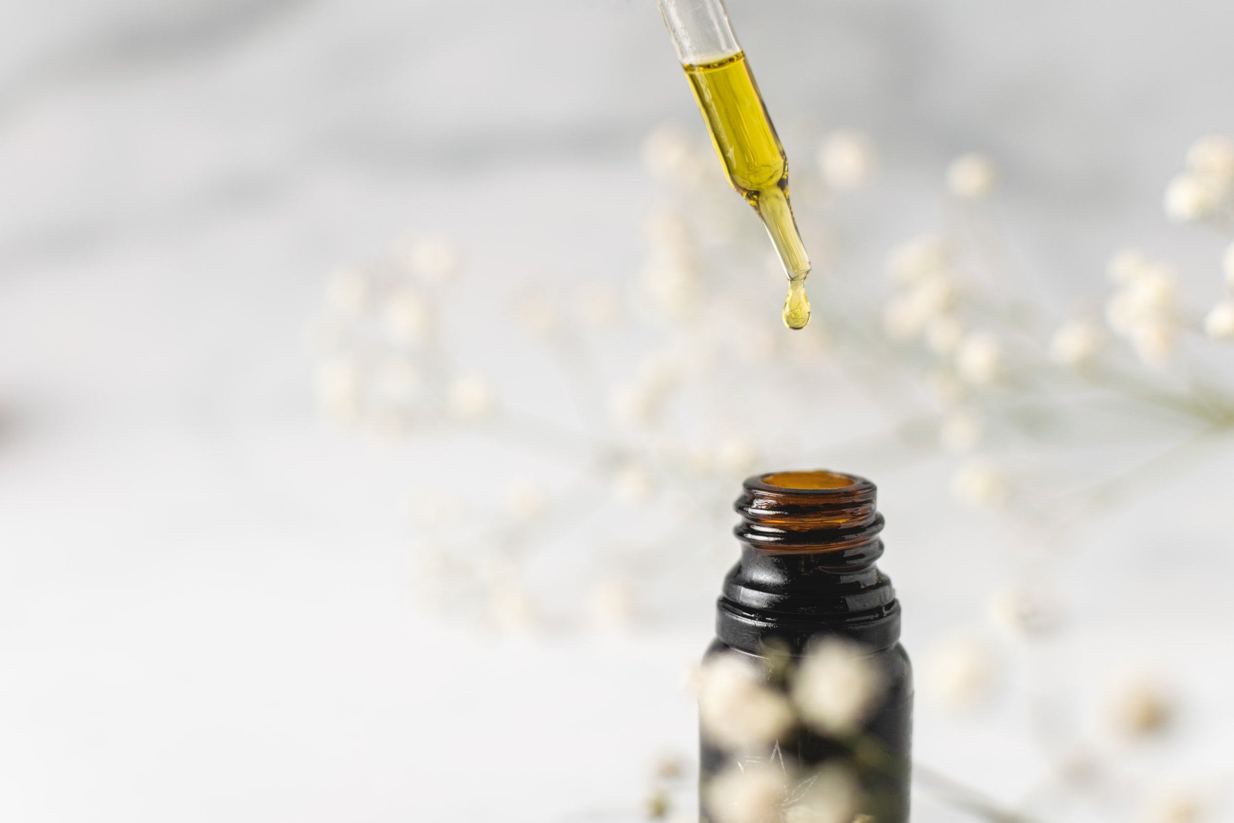 Microdosing mit CBD – sanfte Balance für den Alltag Nahaufnahme einer Pipette mit einem Tropfen CBD-Öl über einer braunen Glasflasche, im Hintergrund zarte, weiße Trockenblumen.