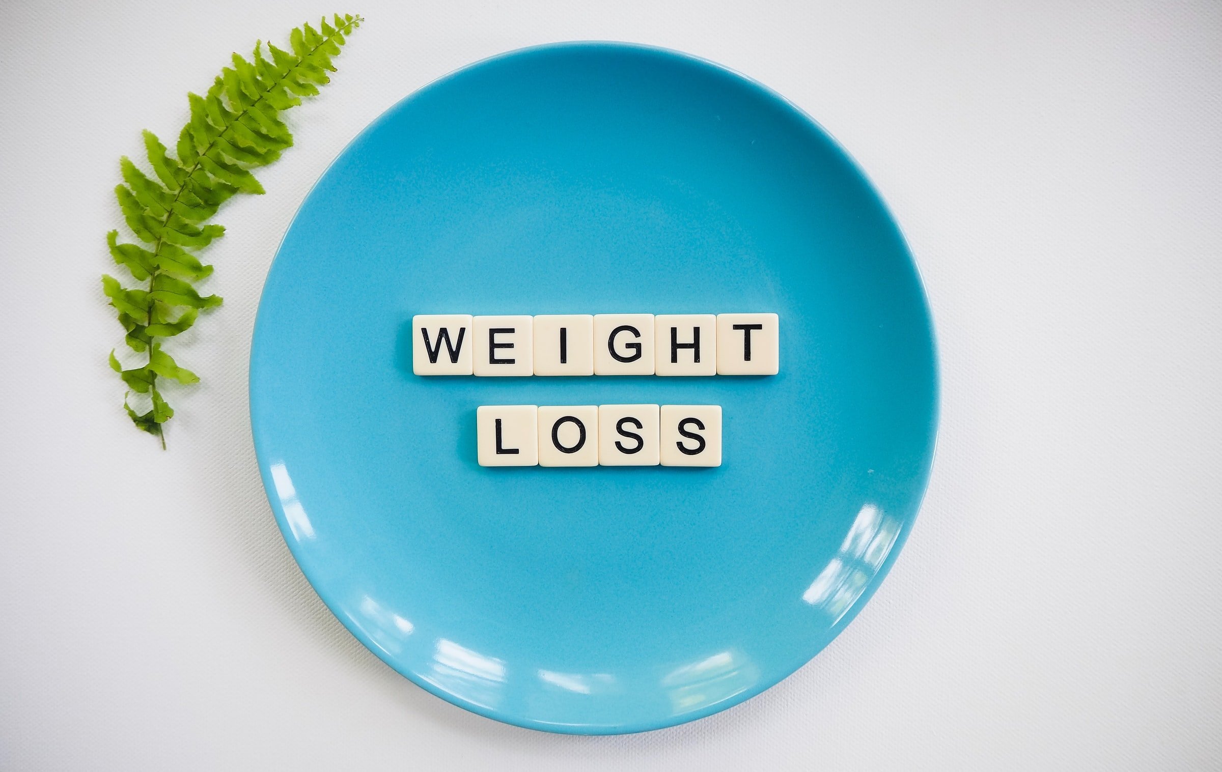 Abnehmen mit CBD – Gewichtsreduktion natürlich unterstützen Blauer Teller mit Buchstabenwürfeln, die das Wort „Weight Loss“ (Gewichtsverlust) bilden – symbolisiert gesunde Ernährung und Diät.