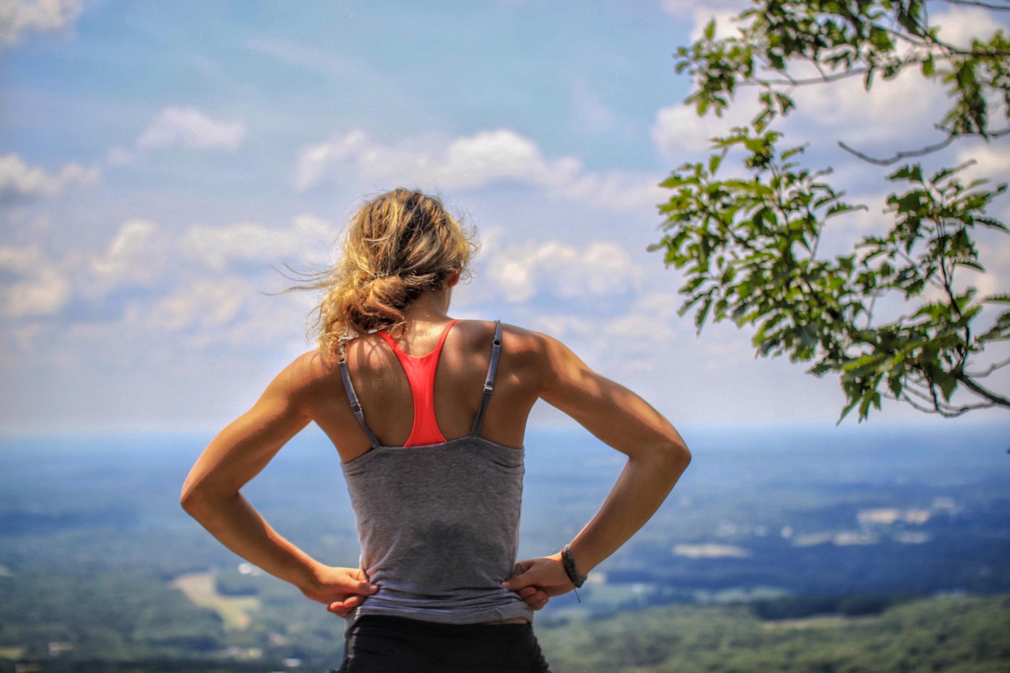 CBD für Muskelregeneration – Erholung nach dem Training in Einklang mit der Natur Sportlich aktive Frau mit Blick ins Tal nach einer Wanderung – steht für Regeneration und Erholung durch CBD nach dem Sport