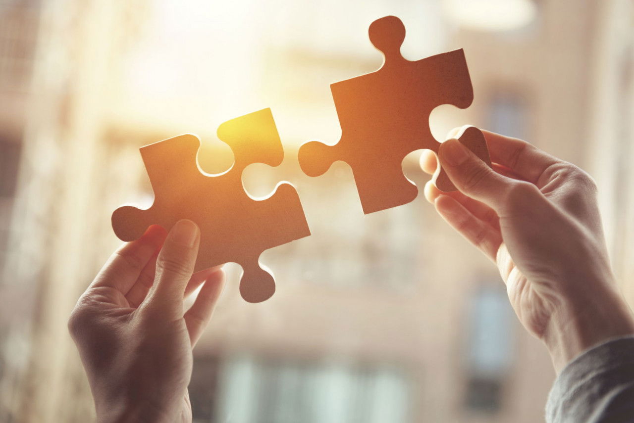 Zwei Hände halten passende Puzzleteile vor hellem Hintergrund