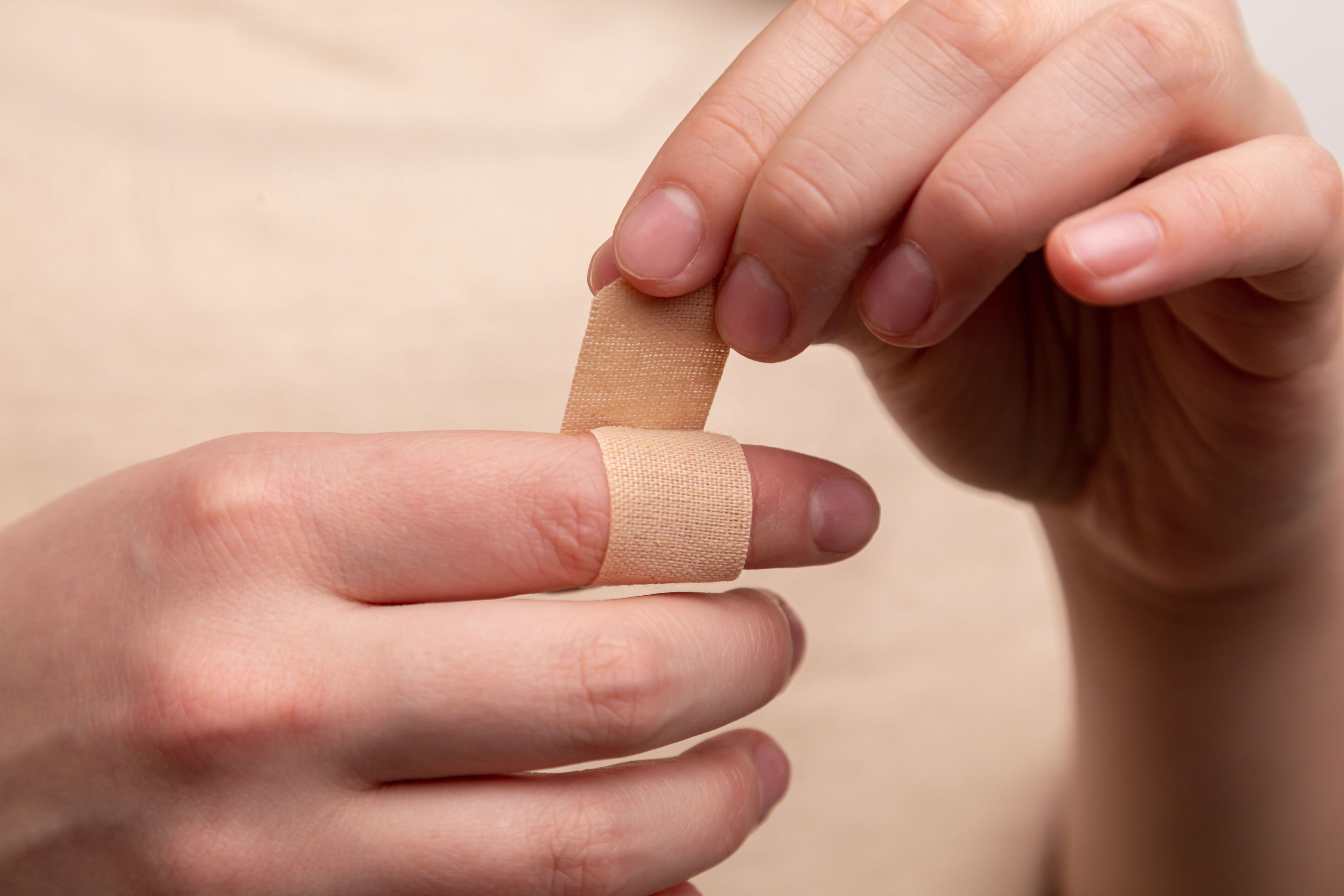 Subjektives Schmerzempfinden – Schmerz ist, was du fühlst Nahaufnahme zweier Hände, eine davon wickelt ein hautfarbenes Pflaster um den verletzten Finger der anderen Hand – Symbol für Schmerz, Verletzung und Heilung.