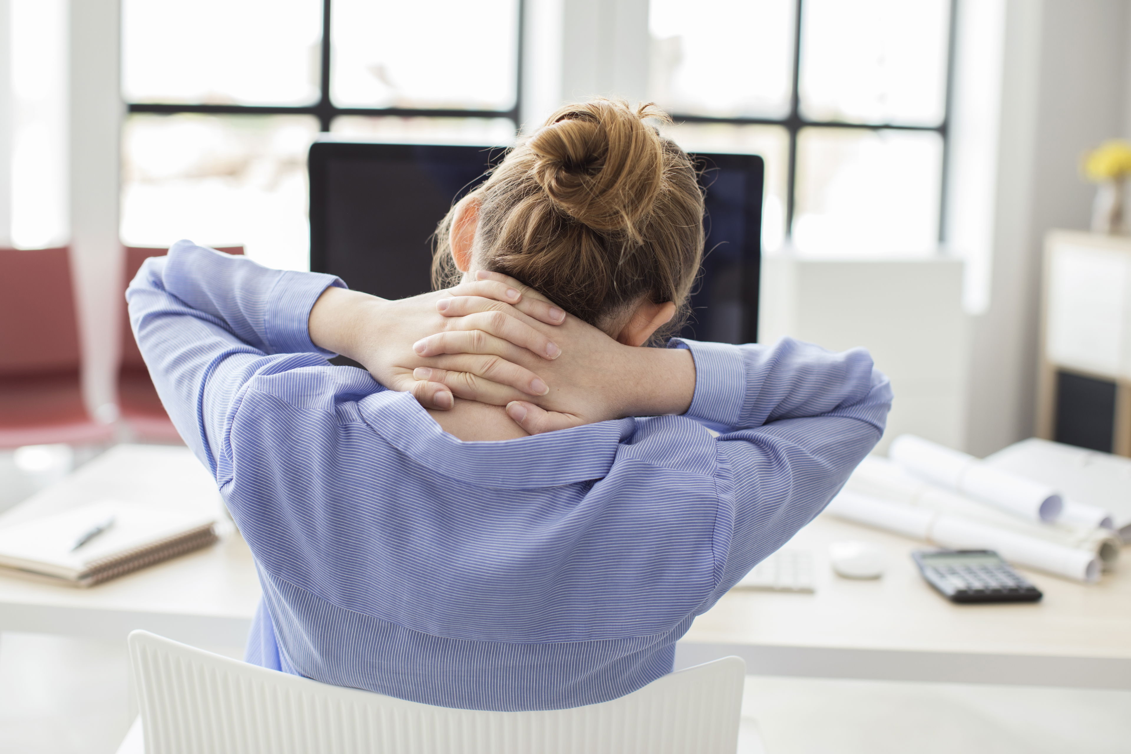Frau sitzt am Schreibtisch und hält sich den Nacken – Symbolbild für Nackenverspannungen oder HWS-Syndrom im Büroalltag.