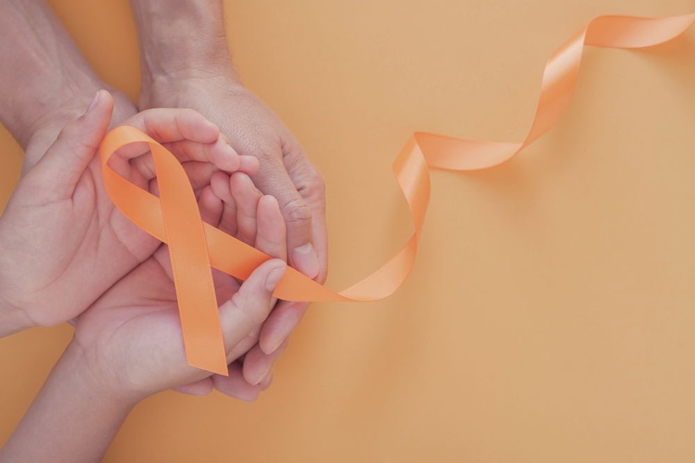 CBD bei Multipler Sklerose – Symbolbild mit oranger Schleife Orangene Schleife, gehalten von mehreren Händen auf orangem Hintergrund – Symbol für Unterstützung und Bewusstsein bei Multipler Sklerose (MS).