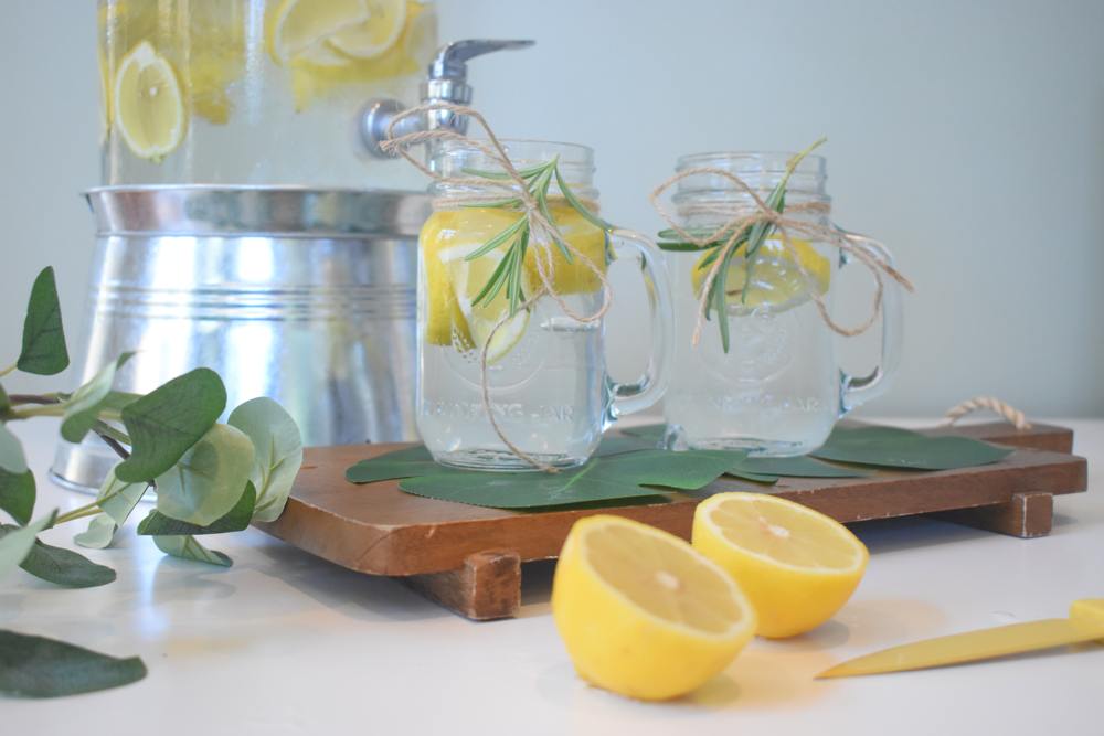 Detox mit CBD – frischer Start für Körper und Geist Zwei Gläser mit Zitronenwasser und Rosmarin auf einem Holztablett neben einer angeschnittenen Zitrone – Symbolbild für Entgiftung mit CBD