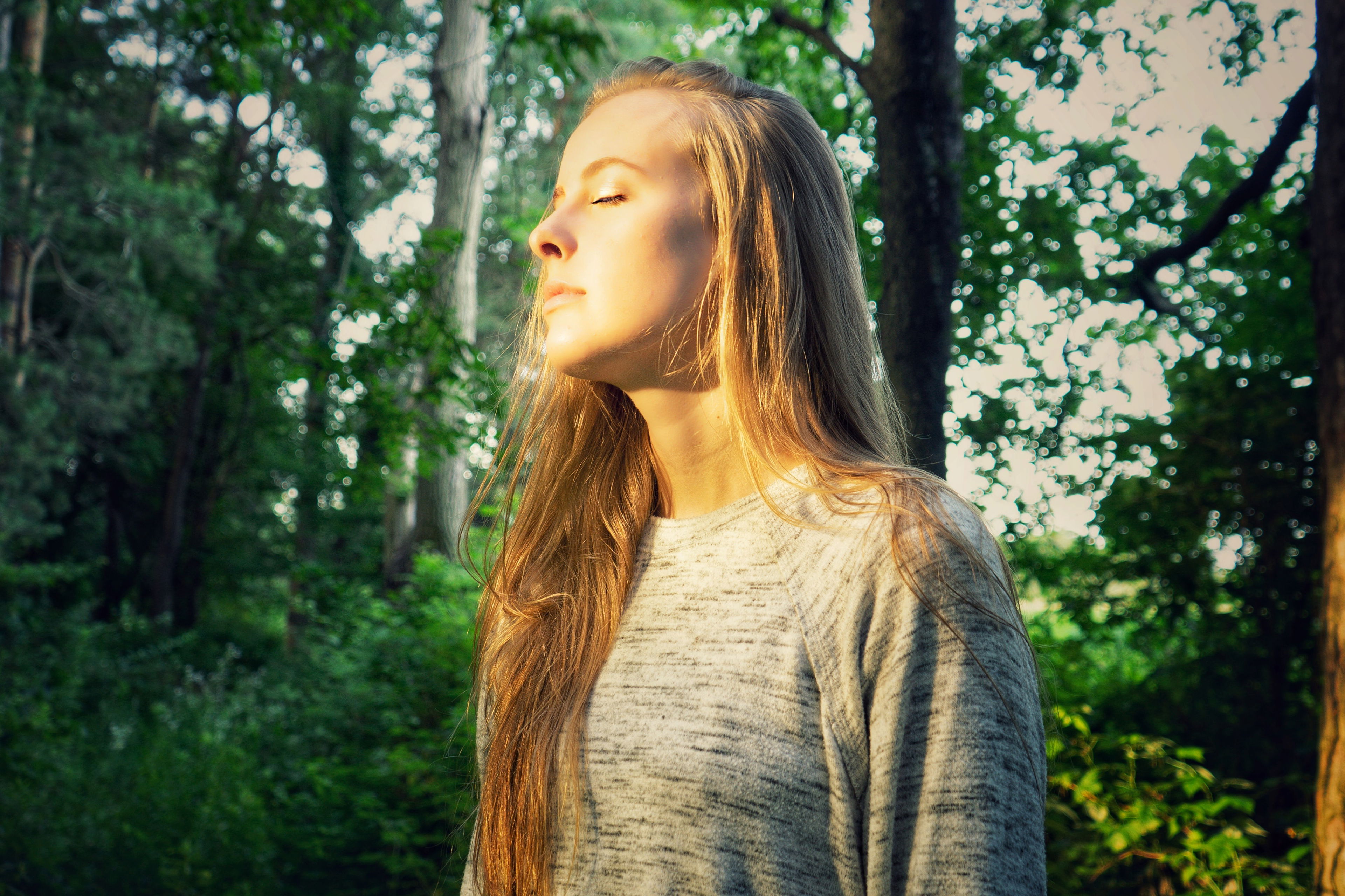 In der Natur zur Ruhe kommen – Abschalten und neue Energie tanken Junge Frau mit geschlossenen Augen steht entspannt im Wald und genießt die Sonne – Symbolbild für Achtsamkeit und Abschalten im Alltag