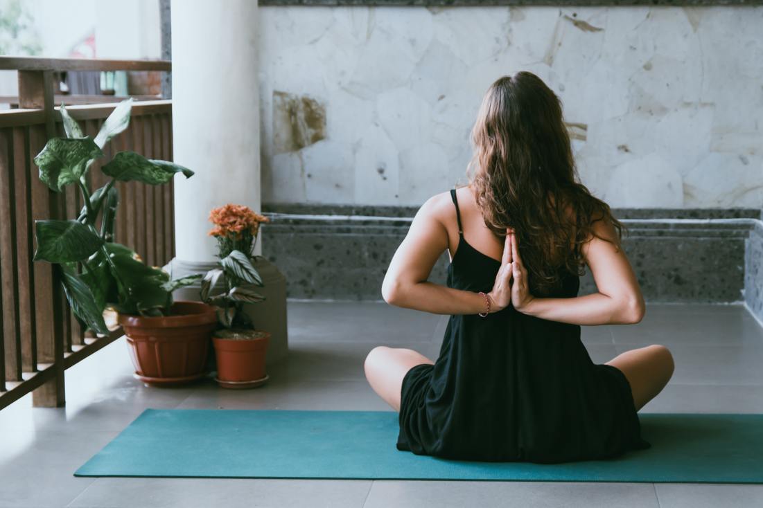 CBD und Yoga – innere Balance für Körper und Geist Frau sitzt im Yogasitz auf einer Matte in Meditationshaltung mit hinter dem Rücken gefalteten Händen – Symbolbild für Achtsamkeit und Entspannung