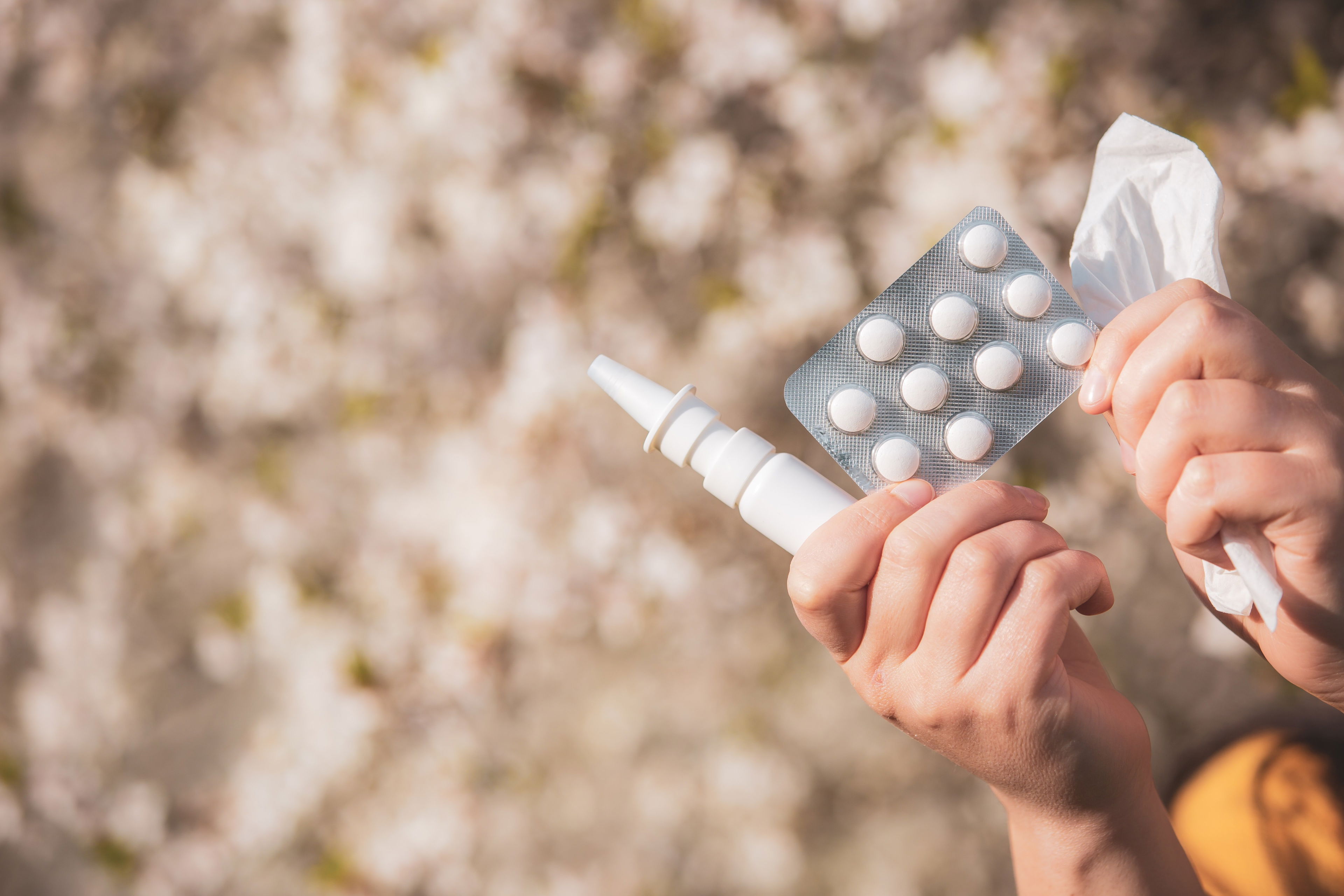 CBD bei Allergien – Alternative zur klassischen Medikation? Zwei Hände halten Antihistaminika in Tablettenform, ein Nasenspray und ein Taschentuch – Symbolbild für typische Allergiebehandlung im Frühling.