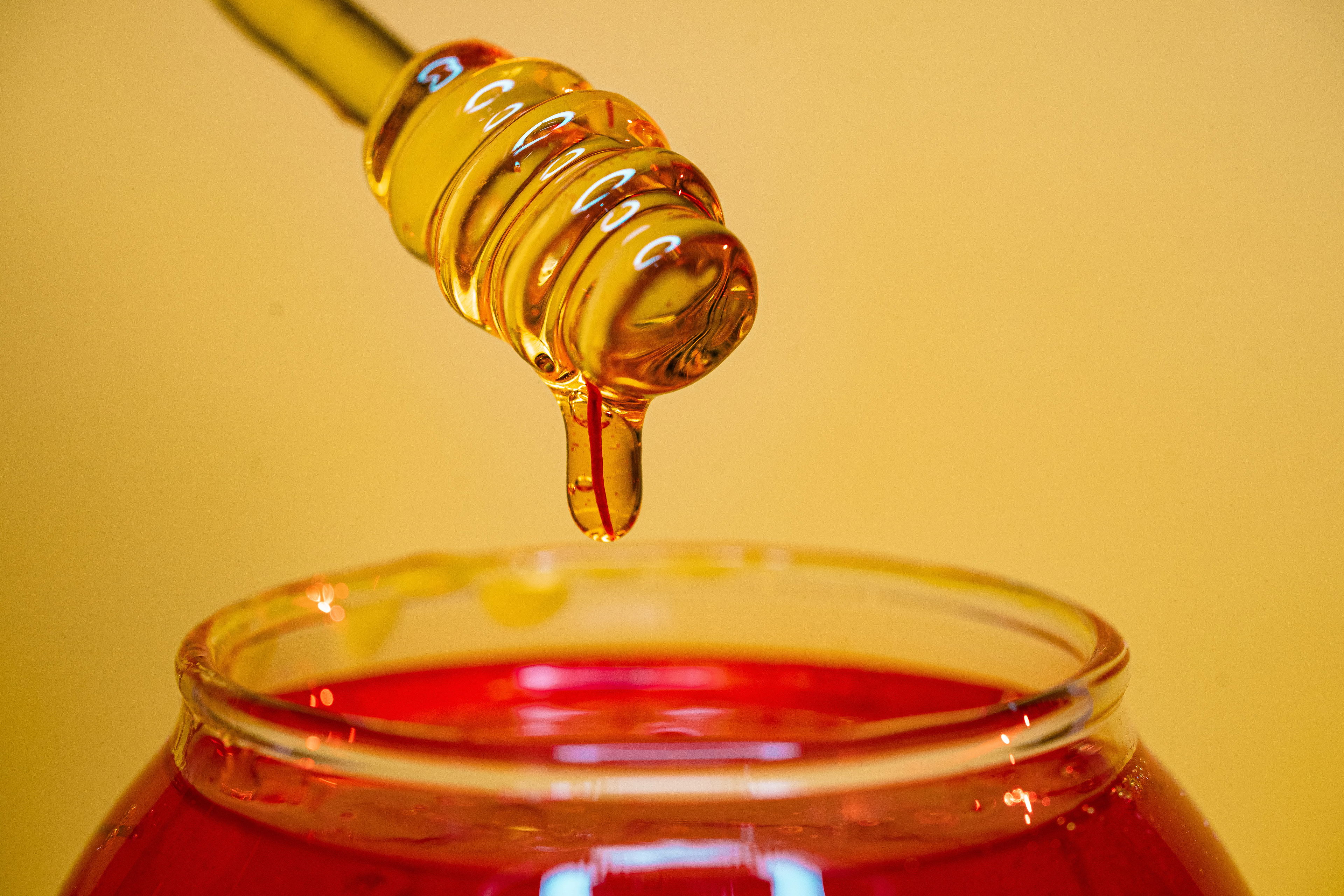 CBD-Honig – süße Verbindung aus Natur und Wirkung Nahaufnahme eines Honiglöffels mit tropfendem goldenen Honig über einem Glas – Symbolbild für CBD-Honig