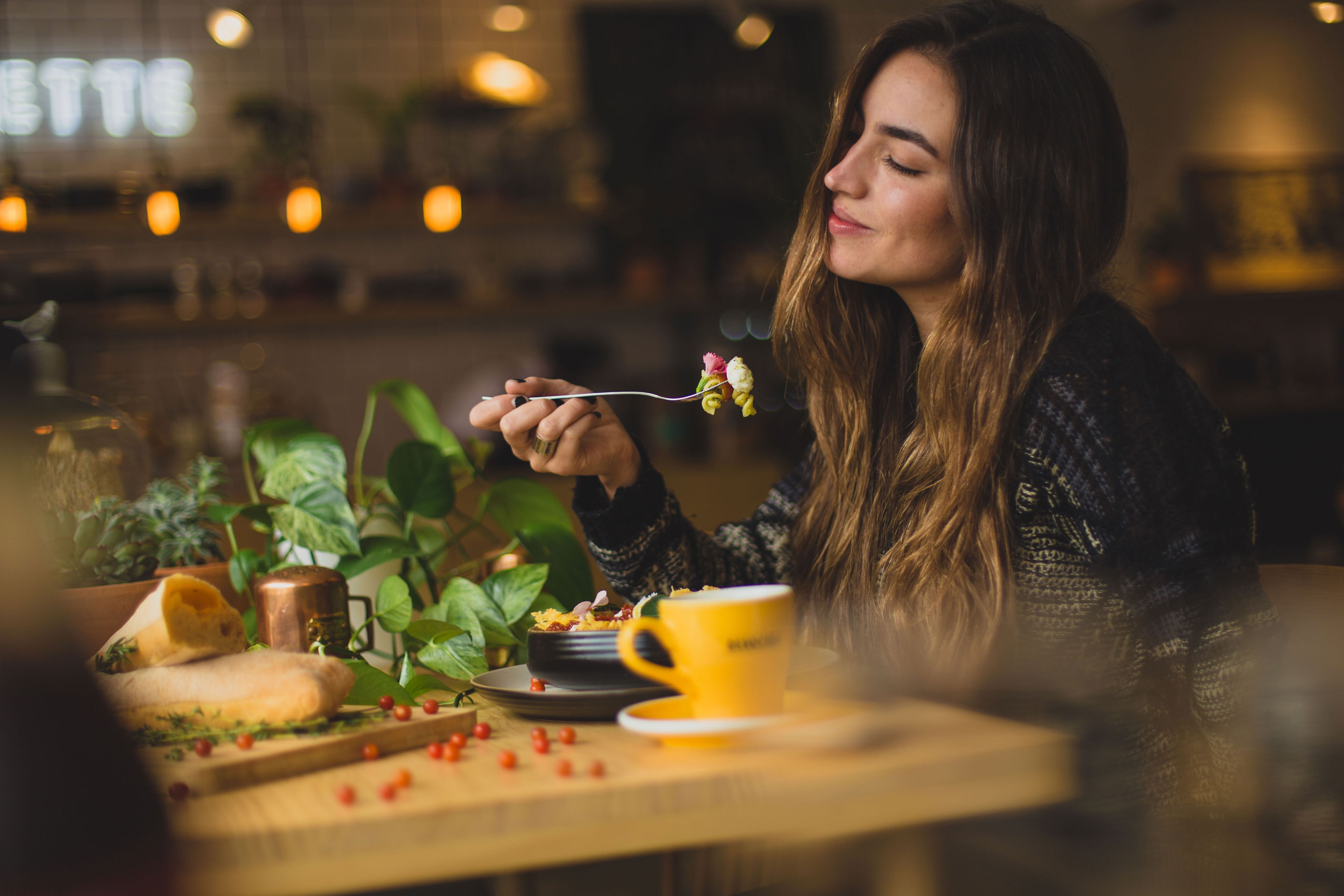 Intuitive Ernährung genießen – Achtsam essen mit CBD Junge Frau genießt achtsam ein Gericht in gemütlicher Café-Atmosphäre – Symbol für intuitive Ernährung mit CBD