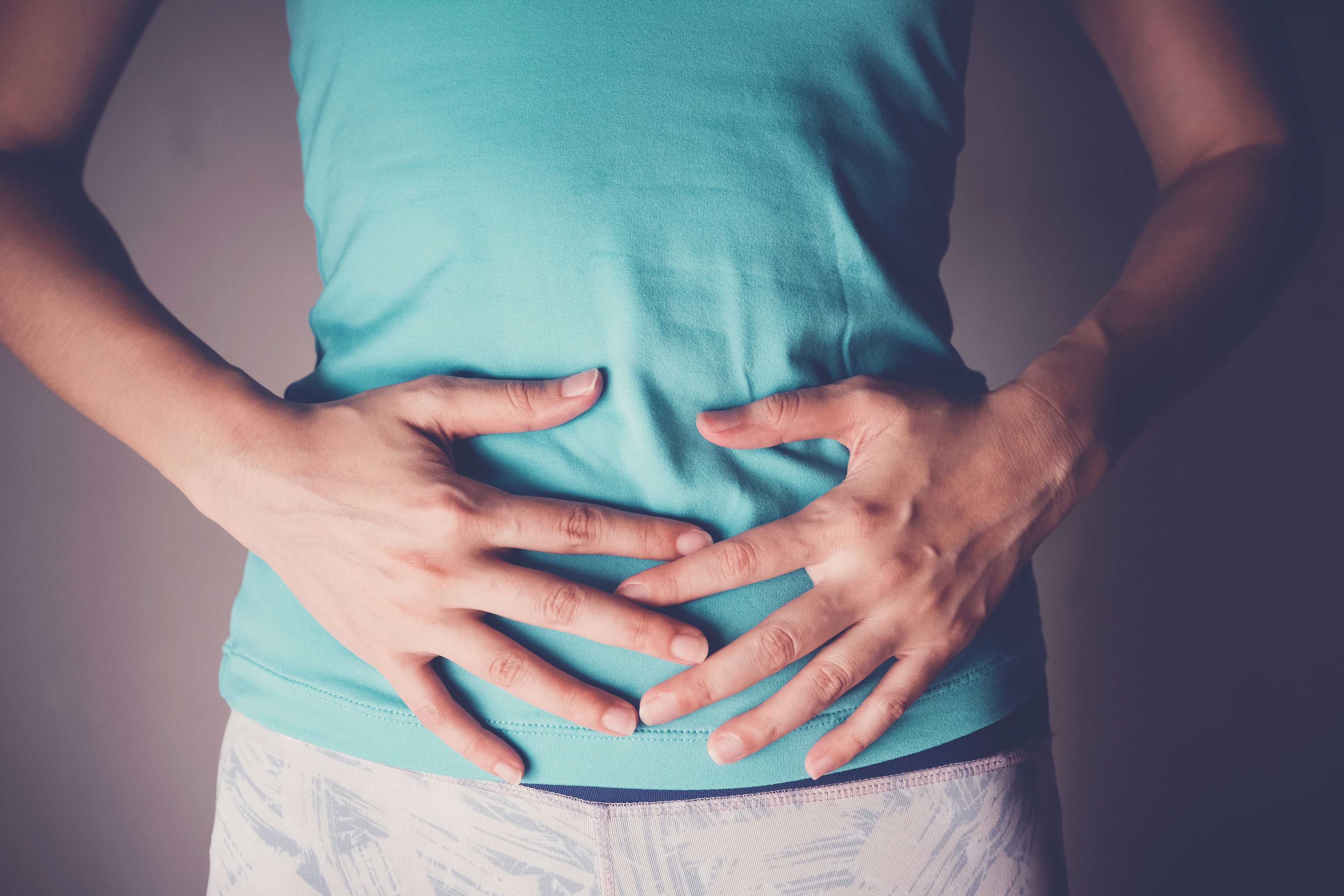 CBD bei Darmkrankheiten – Unterstützung für das Verdauungssystem Person in türkisfarbenem Oberteil hält sich mit beiden Händen den Bauch – Symbolbild für Magen-Darm-Beschwerden.
