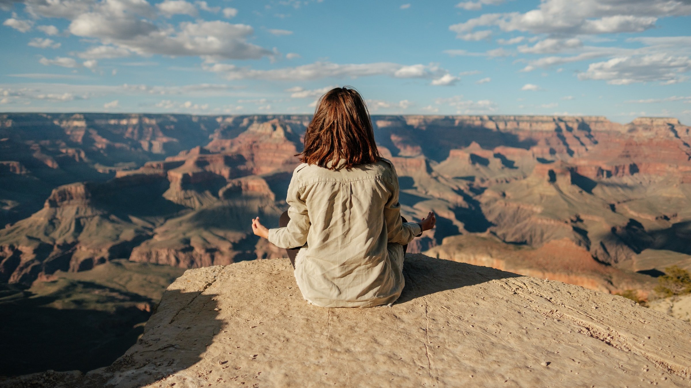CBD und Meditation – Für innere Balance und tiefe Entspannung Frau sitzt in Meditationshaltung auf einem Felsen mit Blick auf eine beeindruckende Canyon-Landschaft, vermutlich Grand Canyon. Die Szene vermittelt Ruhe und Achtsamkeit.